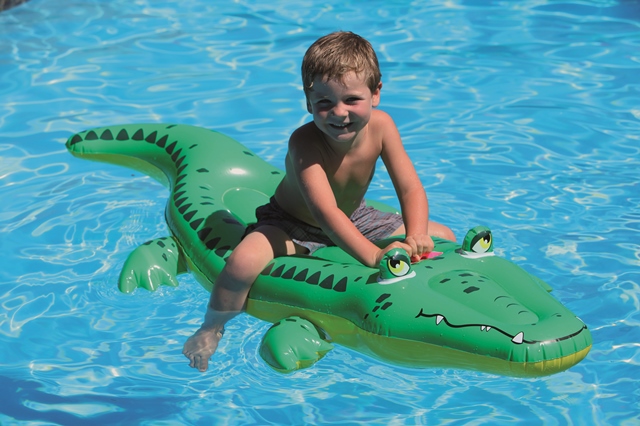 Kind spielt auf einem Schwimmtier in Krokodilform im Pool.