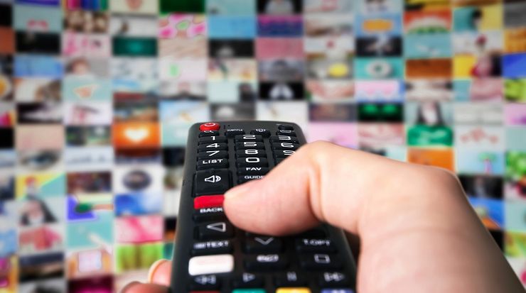 Hand, die eine Fernbedienung hält, im Hintergrund viele Broadcastin-Apps