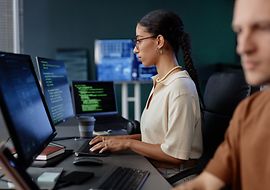 Zwei Personen sitzen vor ihren PCs und sichern die Qualität in ihrem Unternehmen