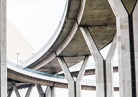 Moderne Betonbrücke mit eleganten Kurven und Seilen vor hellem Himmel