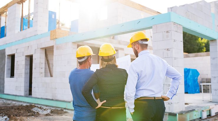 Drei Personen schauen auf einen Bauplan auf einer Baustelle