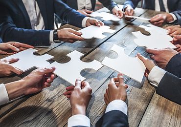 Menschen sitzen um einen Tisch und halten Puzzleteile in der Hand