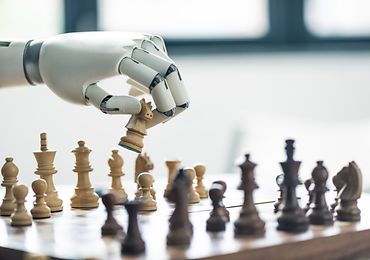 Roboterarm über einem Schachbrett. Der Roboter hält eine Spielfigur in der Hand.