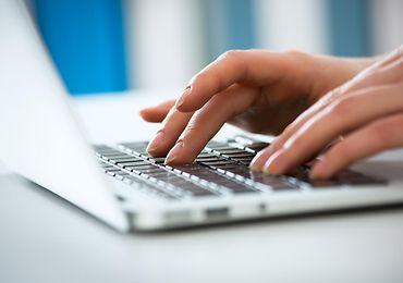 Nahaufnahme von zwei Händen, die auf einem Laptop tippen